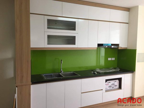 Tủ bếp Melamine màu trắng điểm nhấn là kính ốp bàn bếp màu xanh.