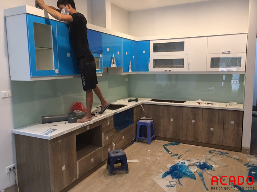 Thợ thi công ACADO đang tiến hành thi công bộ tủ bếp cùng với kính bếp màu trắng xanh cho gia chủ
